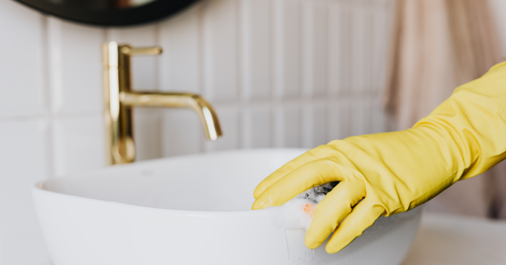 yellow rubber gloved hand scrubbing bathroom sink